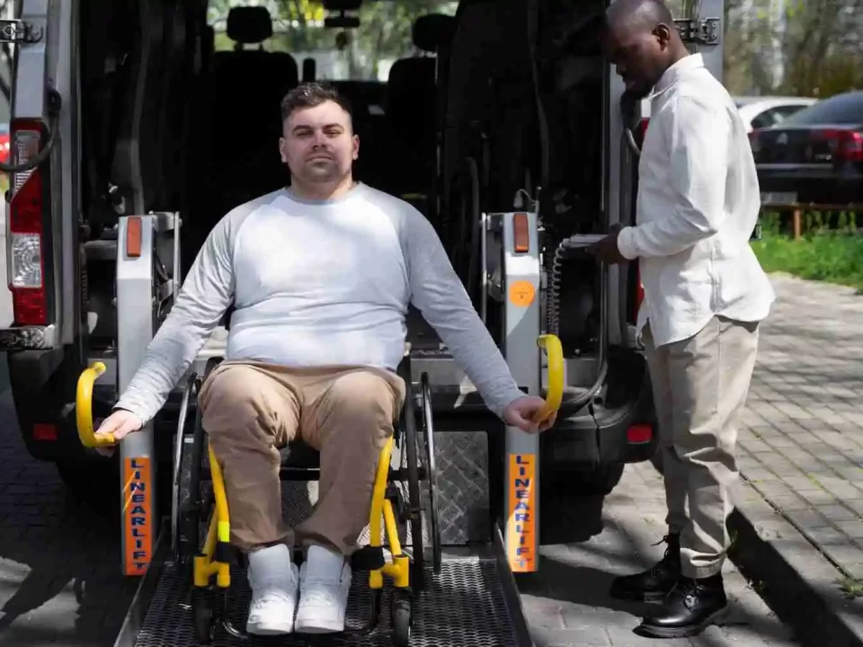 Imagem com um homem em uma cadeira de rodas, descendo de um carro com a ajuda de uma plataforma mecânica.