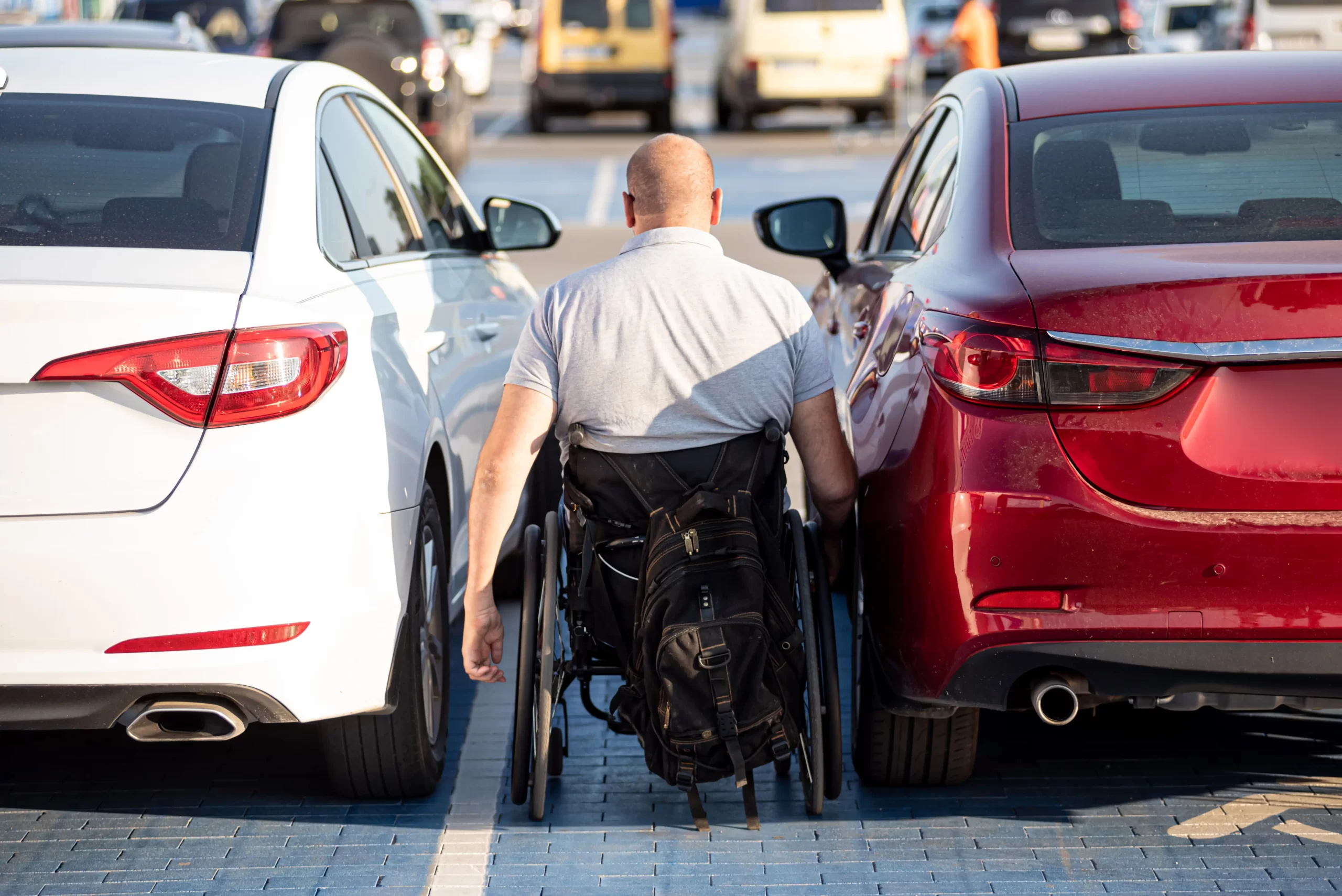 Homem em cadeira de rodas no meio entre dois carros.