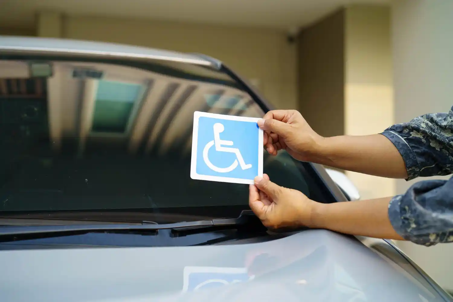 Pessoa aplicando adesivo de identificação PCD com símbolo de cadeira de rodas no para-brisa de carro adaptado